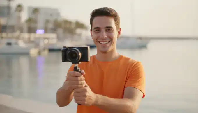 A travel vlogger holding a small camera in a sunny harbor in a travel video for social